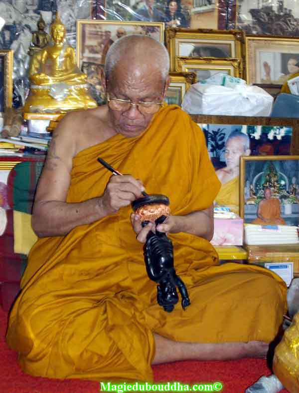 Moine thai qui bénit une statue du Bouddha.
